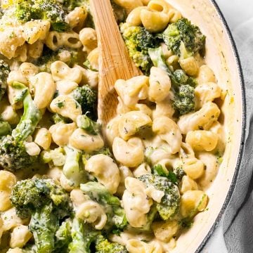 frontal close up view of wooden spoon in pot with creamy broccoli pasta