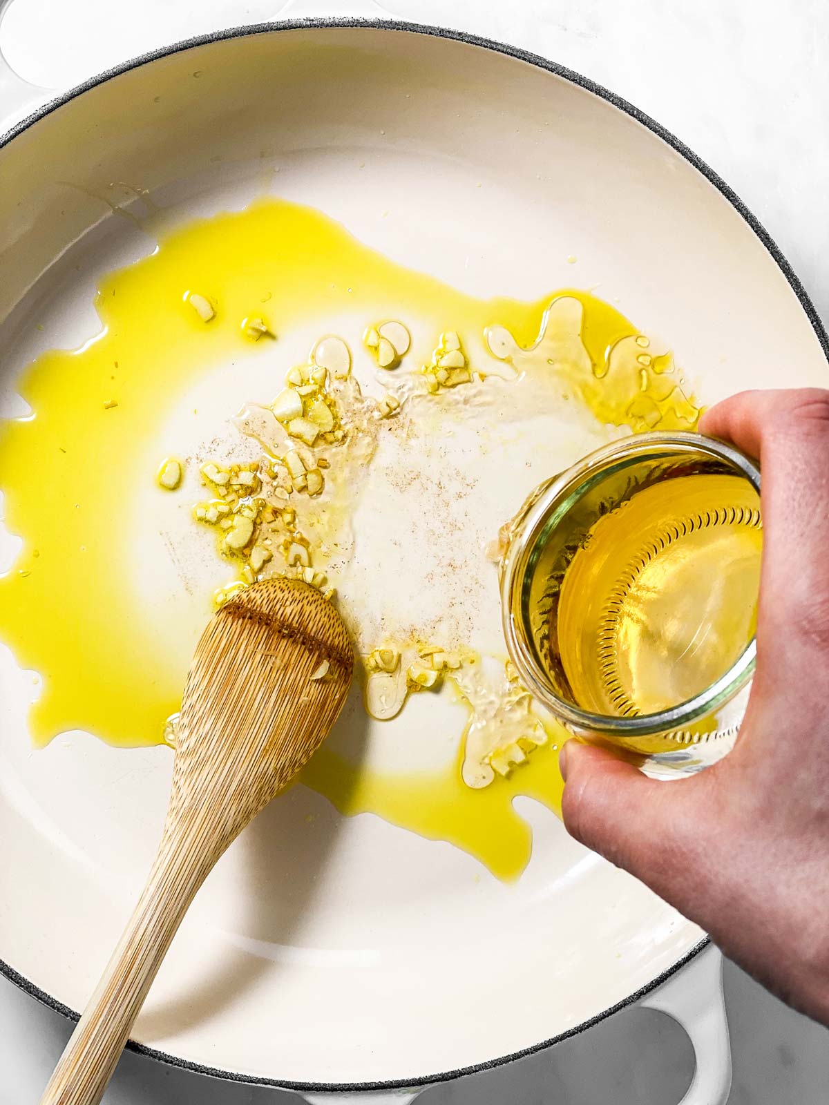 female hand pouring white wine into white skillet with garlic