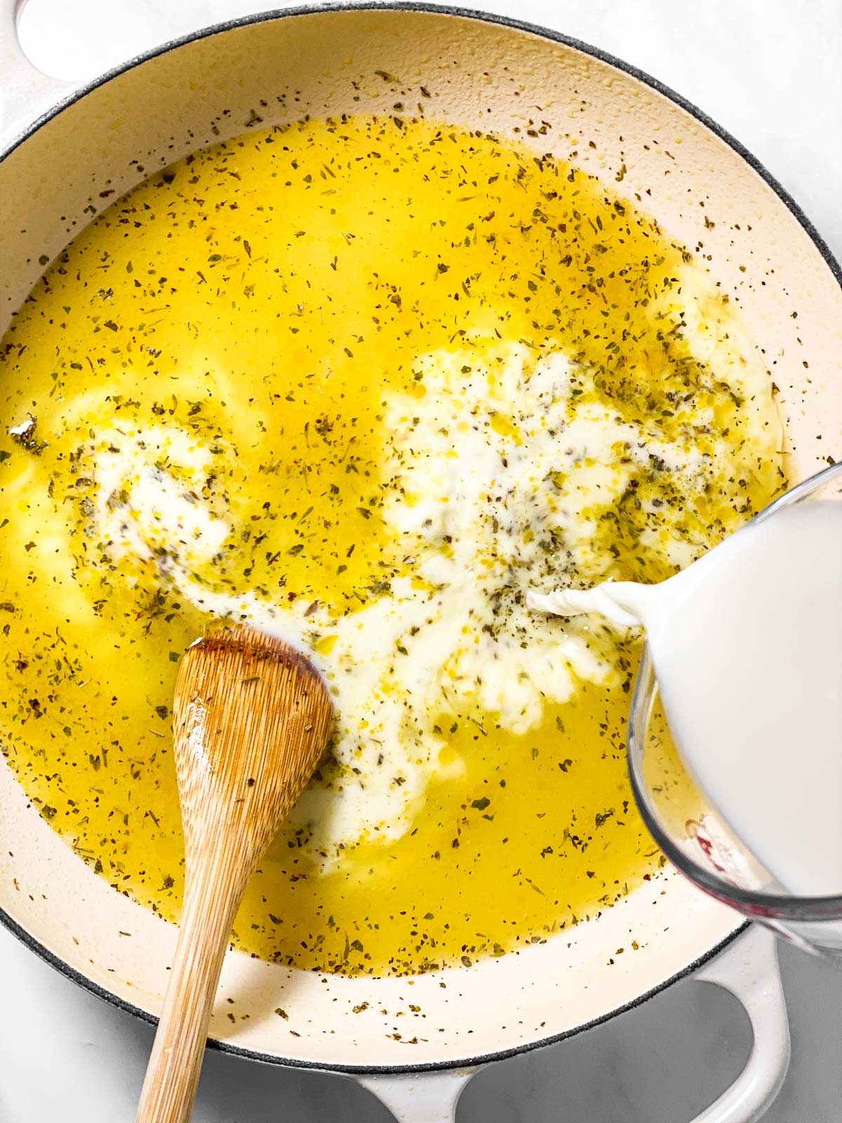 milk pouring from glass measuring jug into white pan with chicken broth