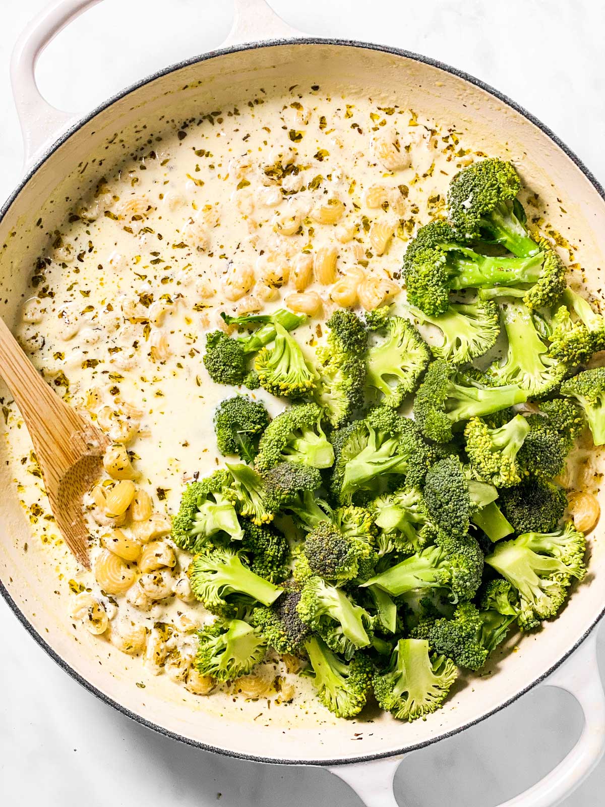 raw broccoli in white skillet with creamy pasta