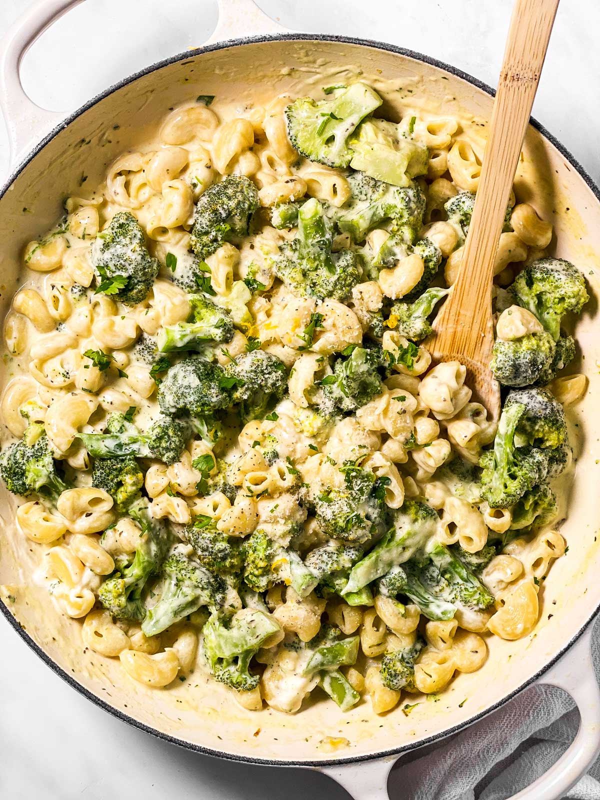 white skillet with broccoli pasta and wooden spoon