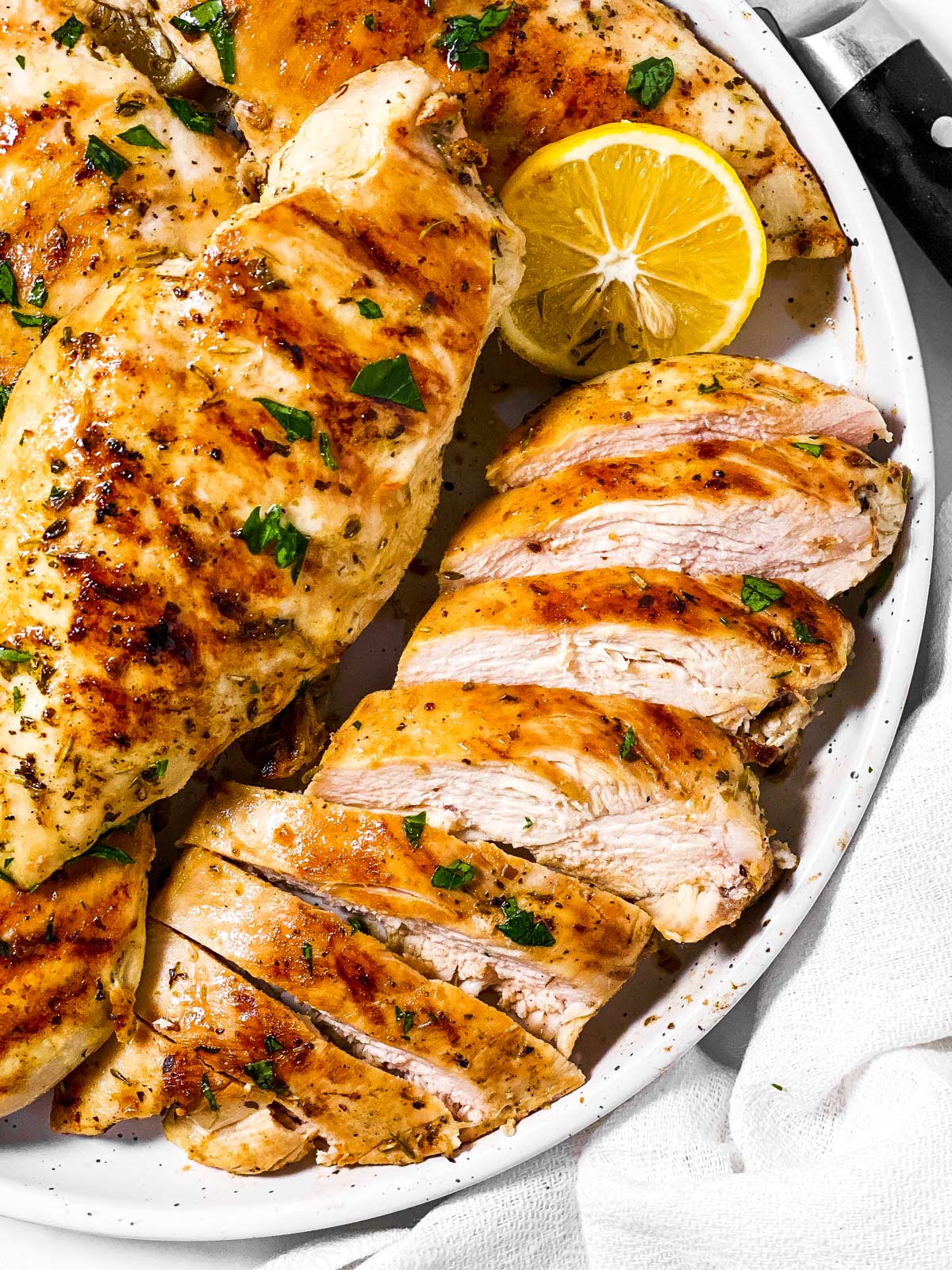 overhead view of sliced grilled chicken breast on plate with several grilled chicken breasts