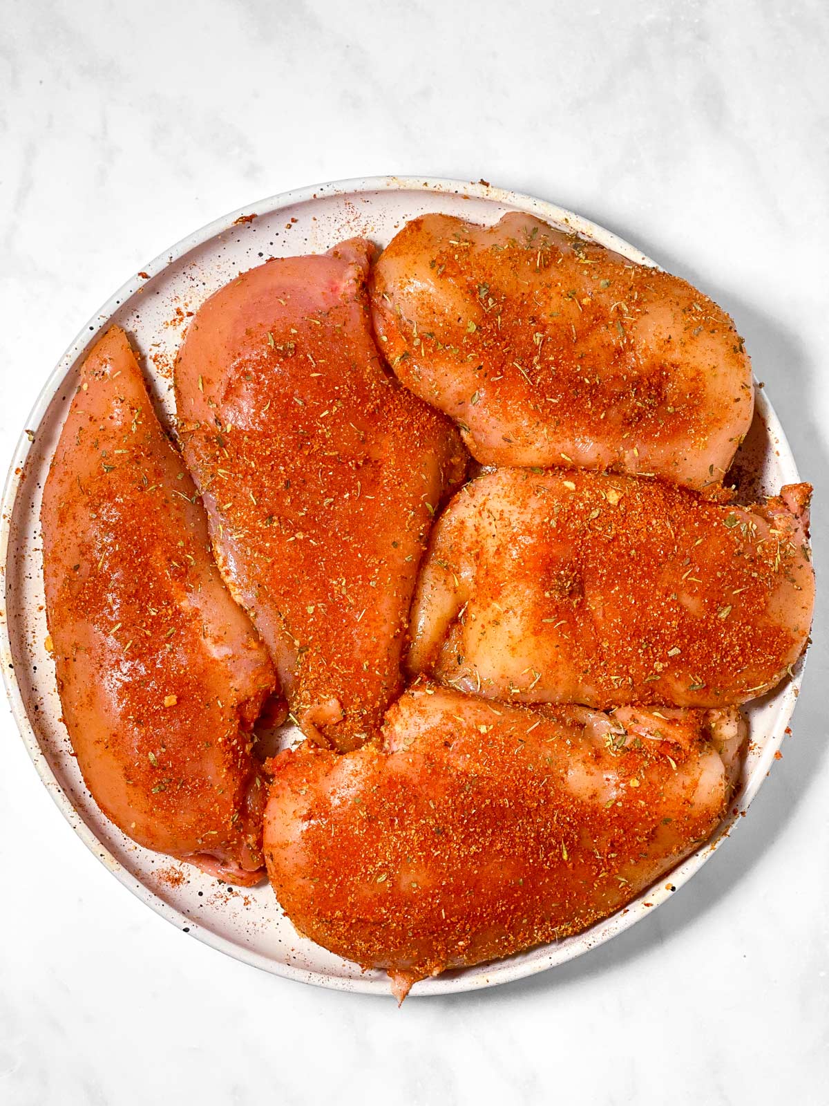 five raw, seasoned chicken breasts on white plate