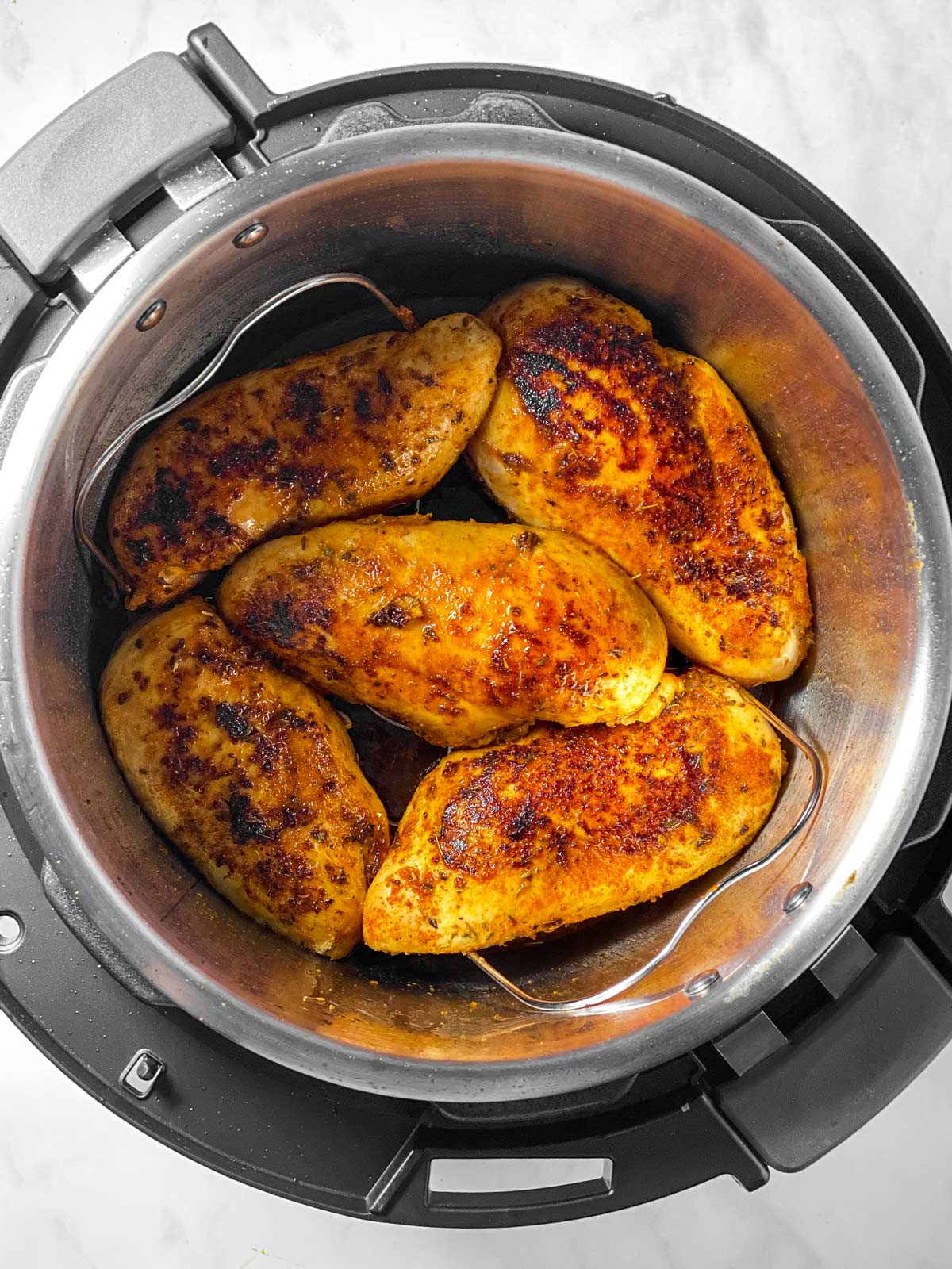 overhead view of five seared chicken breasts on trivet in instant pot