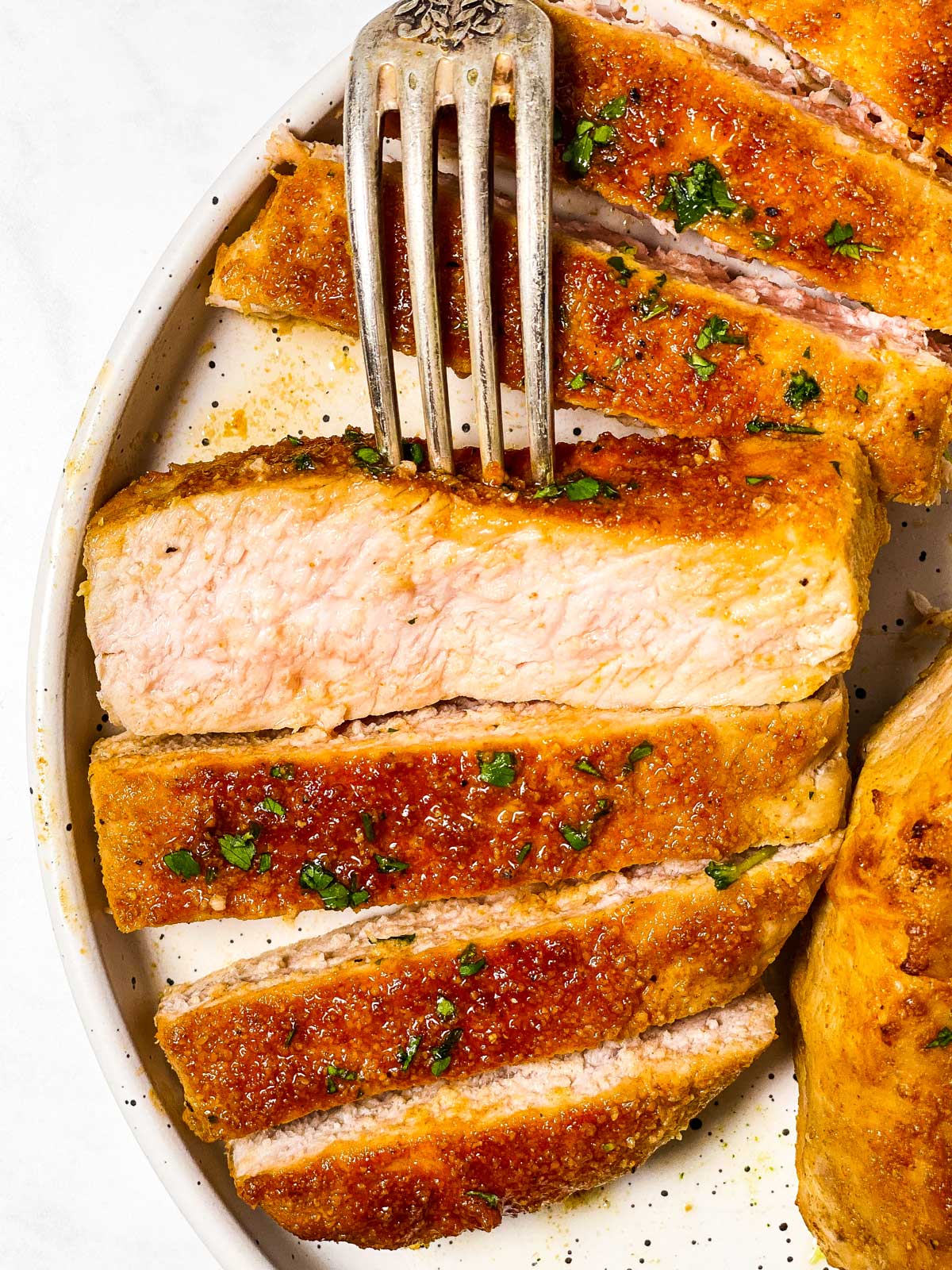 sliced baked pork chop on white plate with fork stuck in one piece