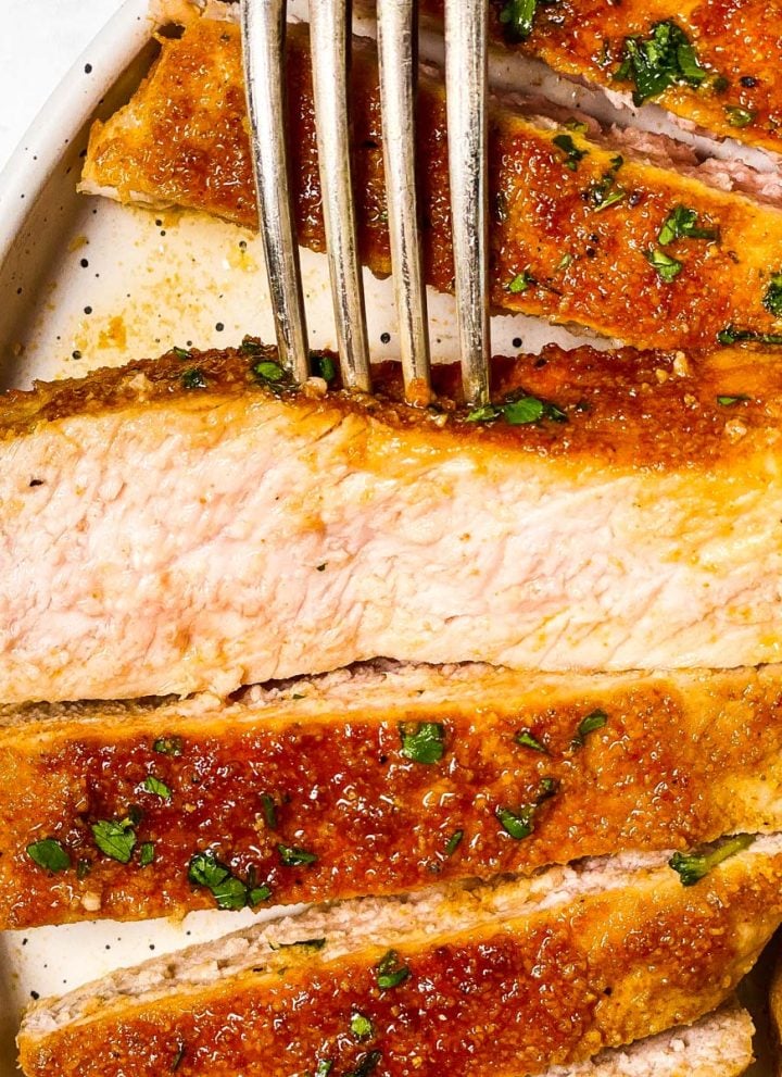 sliced baked pork chop on white plate with fork stuck in one piece