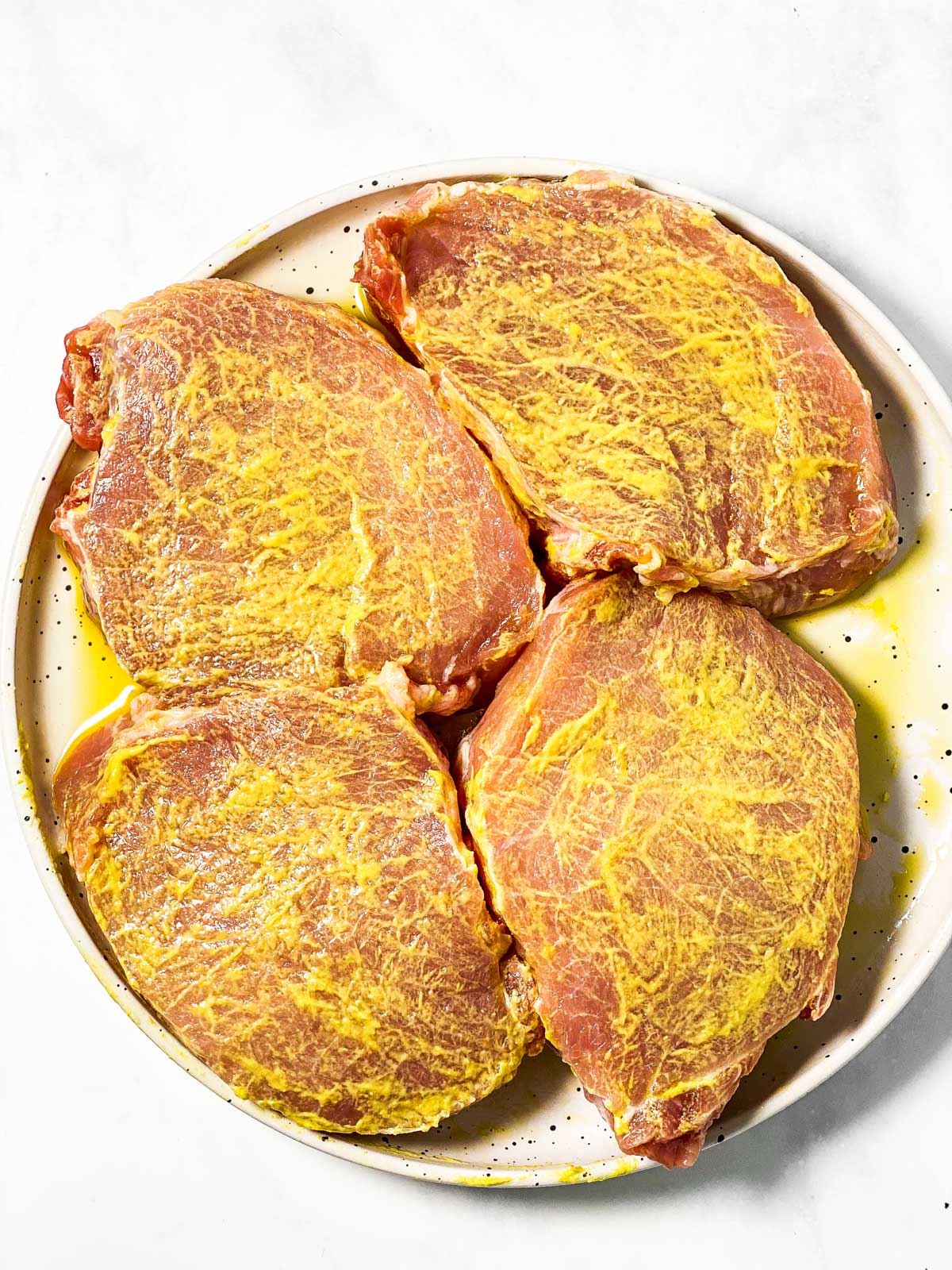 four pork chops covered in mustard on white plate