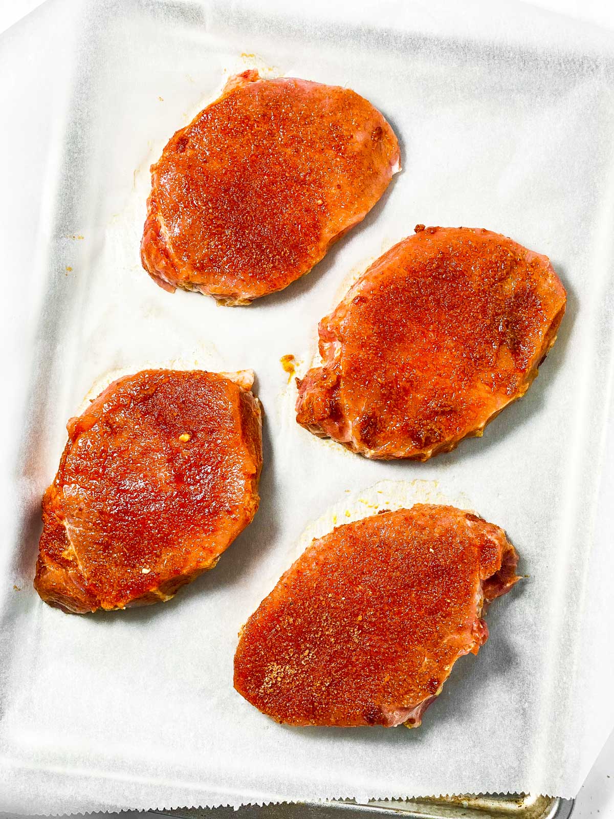 four seasoned pork chops on lined baking sheet