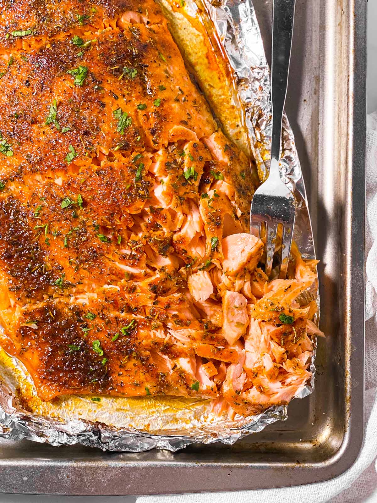 overhead view of oven baked salmon fillet on baking sheet with fork flaking fish