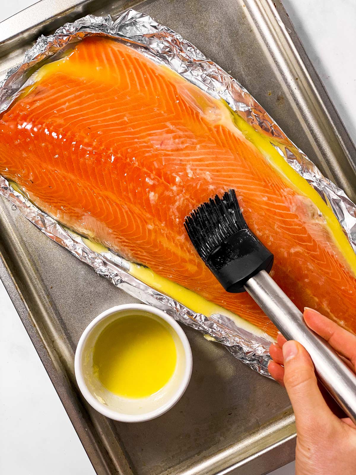 female hand using black silicone brush to brush garlic butter over raw salmon fillet