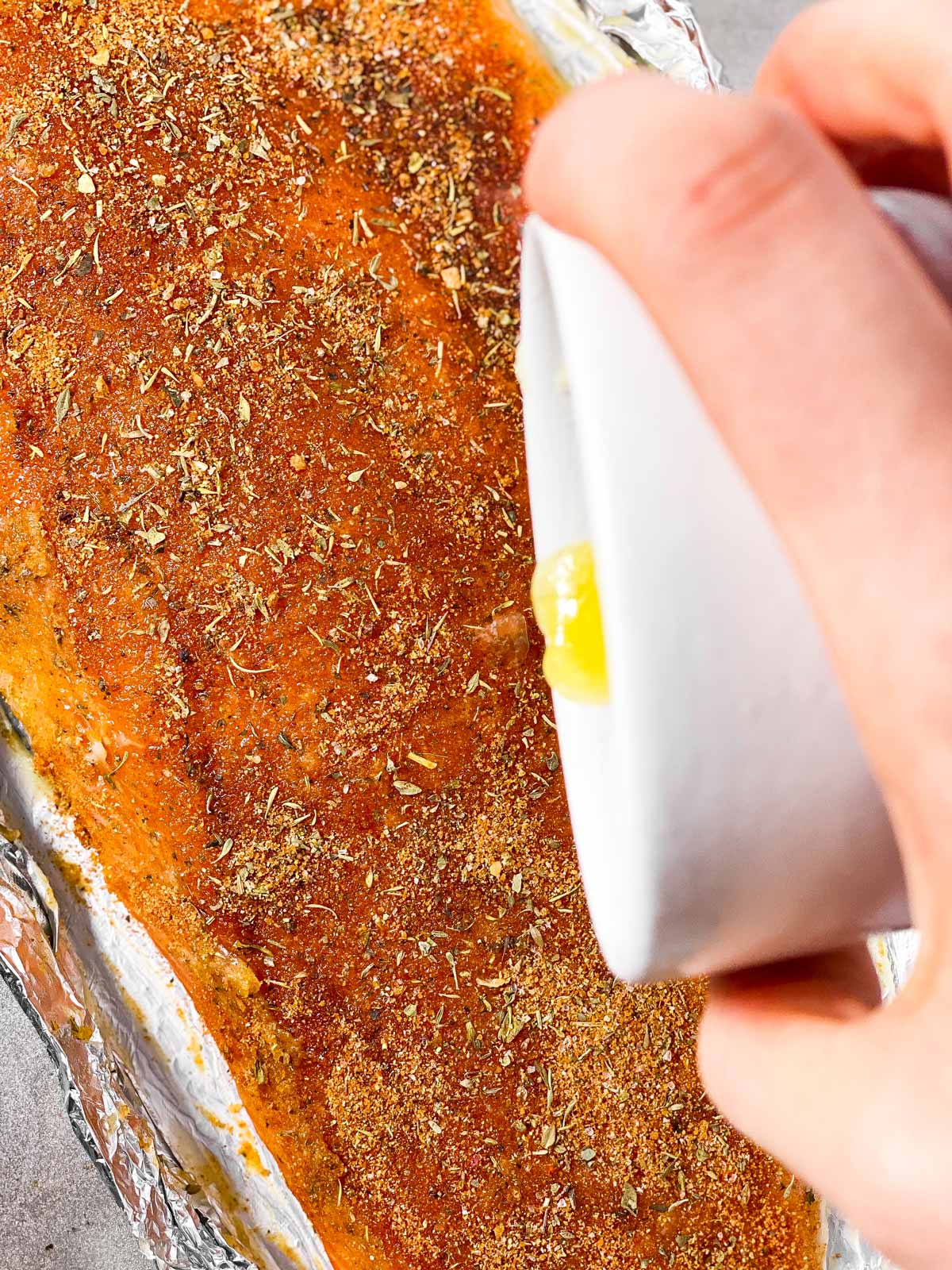 female hand pouring melted butter over seasoned salmon fillet