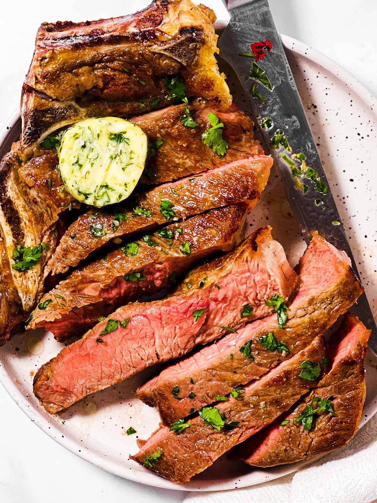 overhead view of sliced steak on white plate with garlic butter