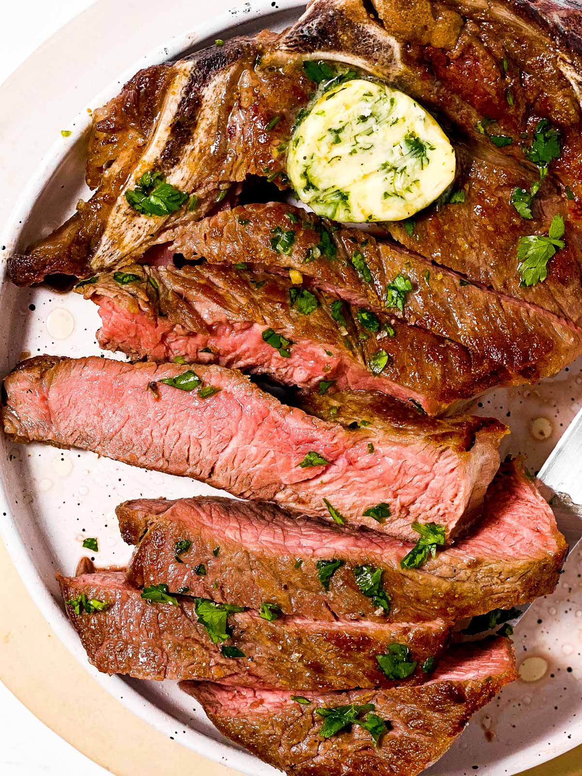 overhead view of sliced steak on white plate with garlic butter