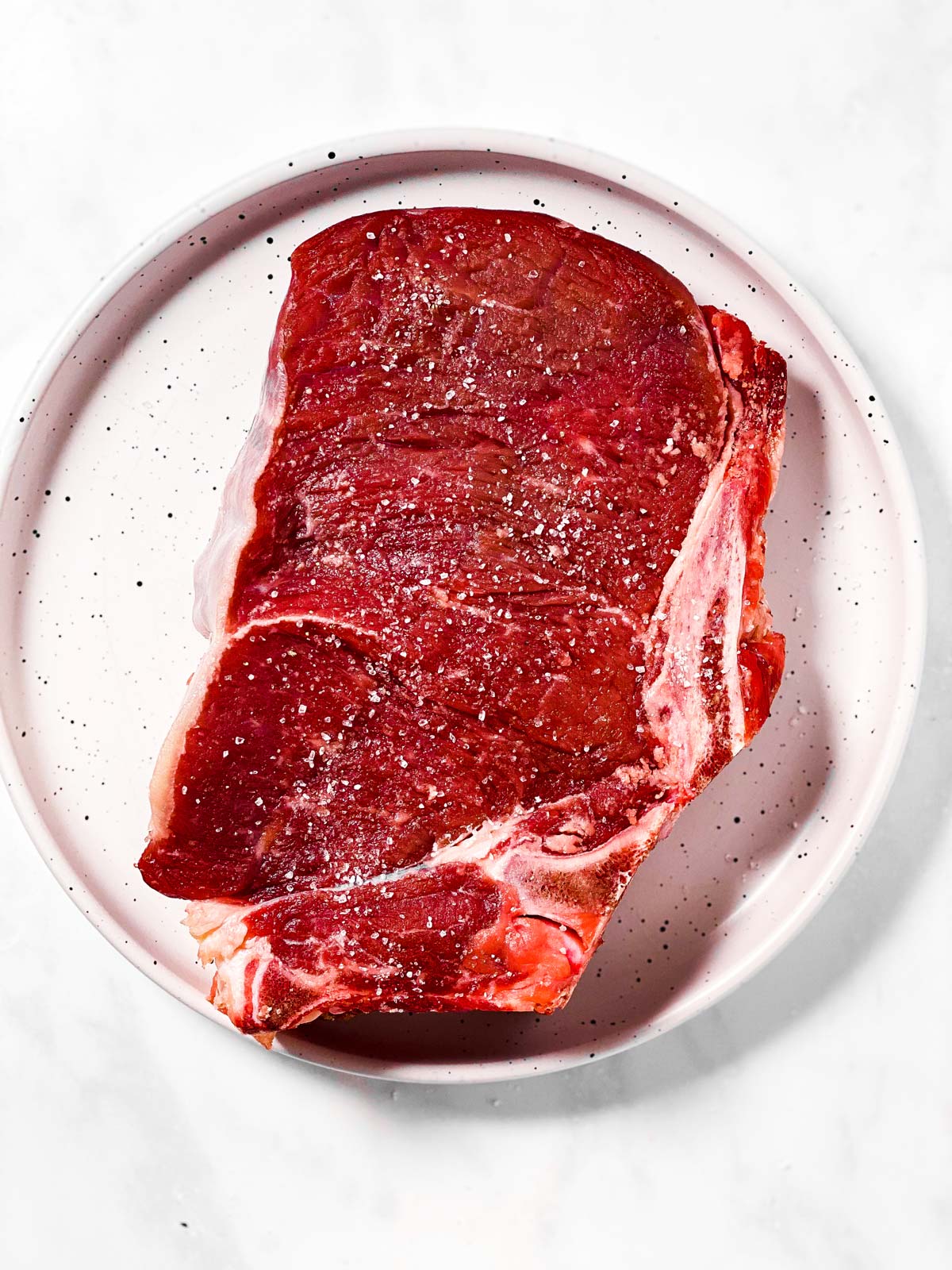 raw seasoned steak on white plate