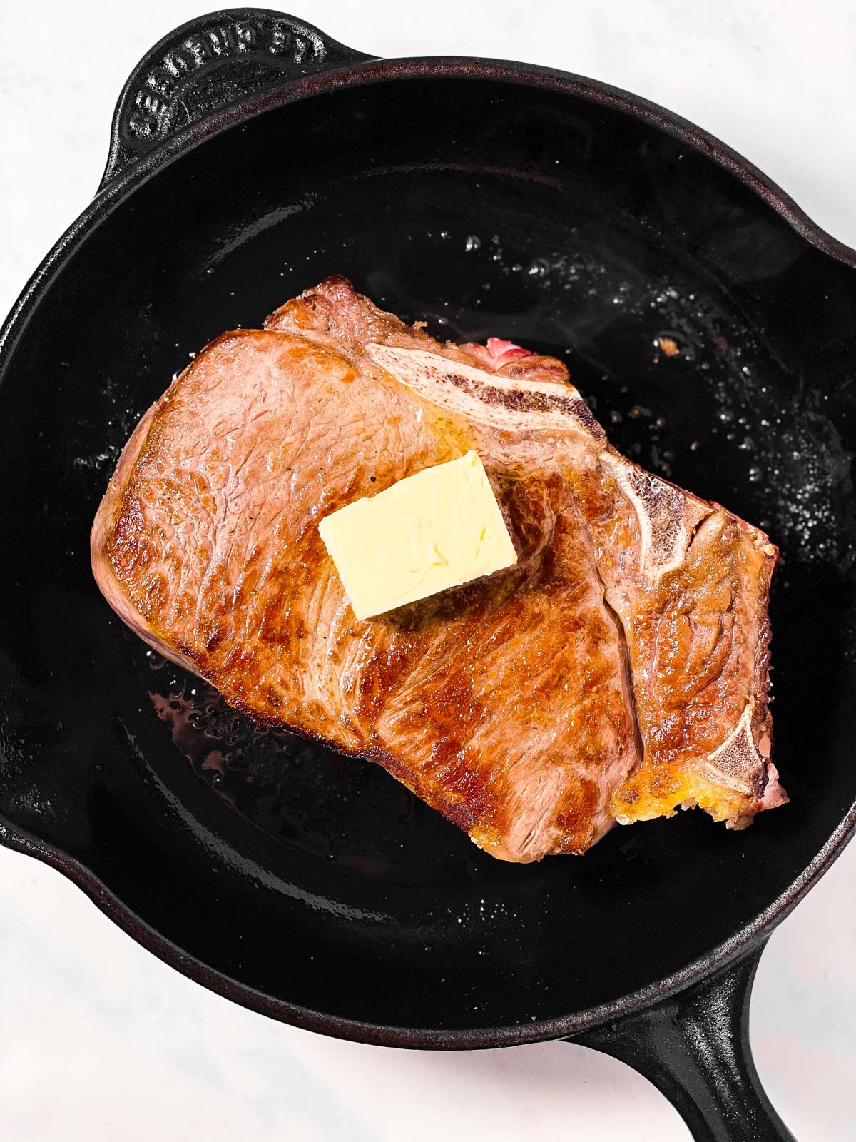 seared steak topped with butter in cast iron skillet