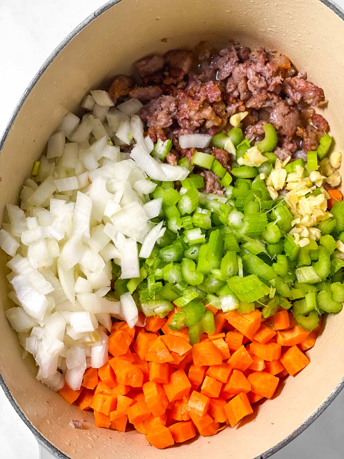 chopped vegetables in oval Dutch oven with browned sausage