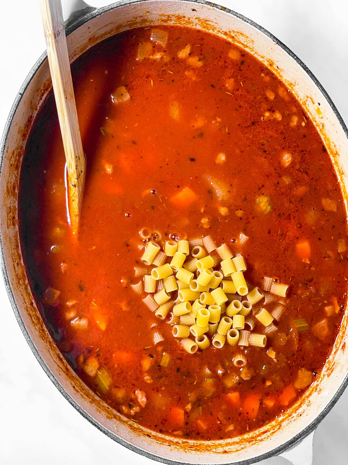 oval Dutch oven filled with soup and uncooked Ditalini pasta