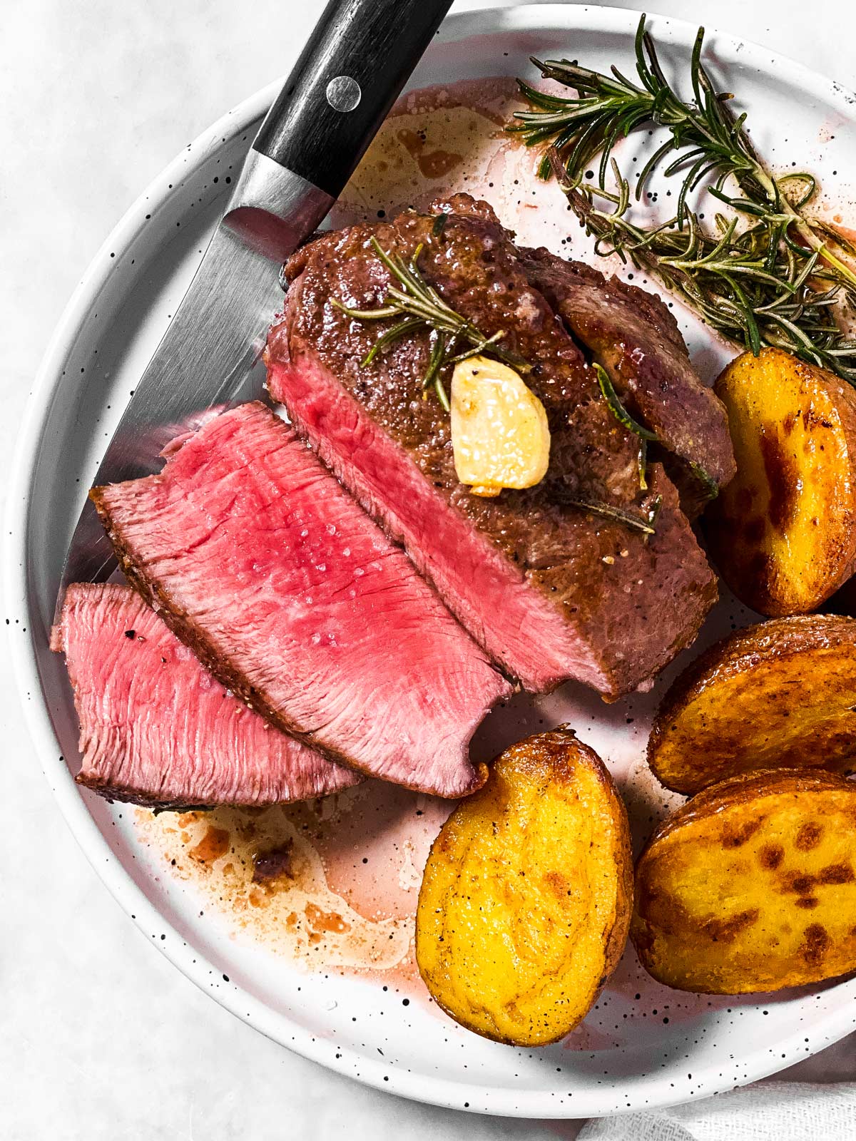 overhead view of sliced filet mignon on white plate with roasted potatoes