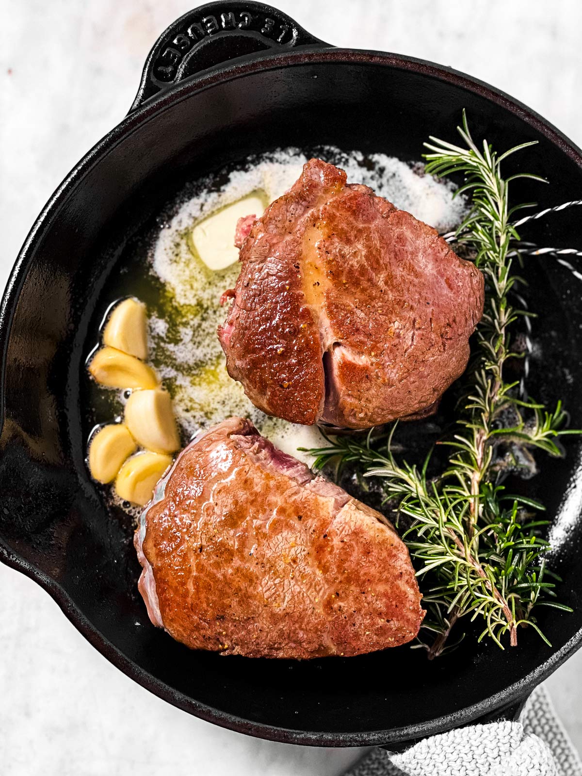 two seared filet mignon steaks in cast iron skillet with butter, garlic and rosemary sprigs