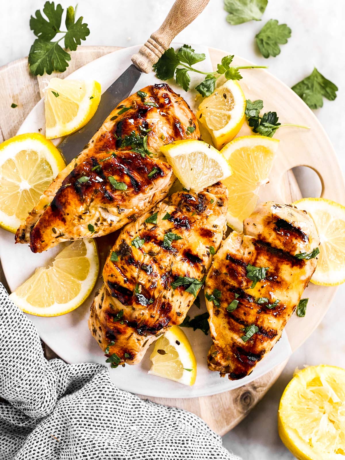 overhead view of three Greek grilled chicken breasts in platter with lemon and fresh parsley