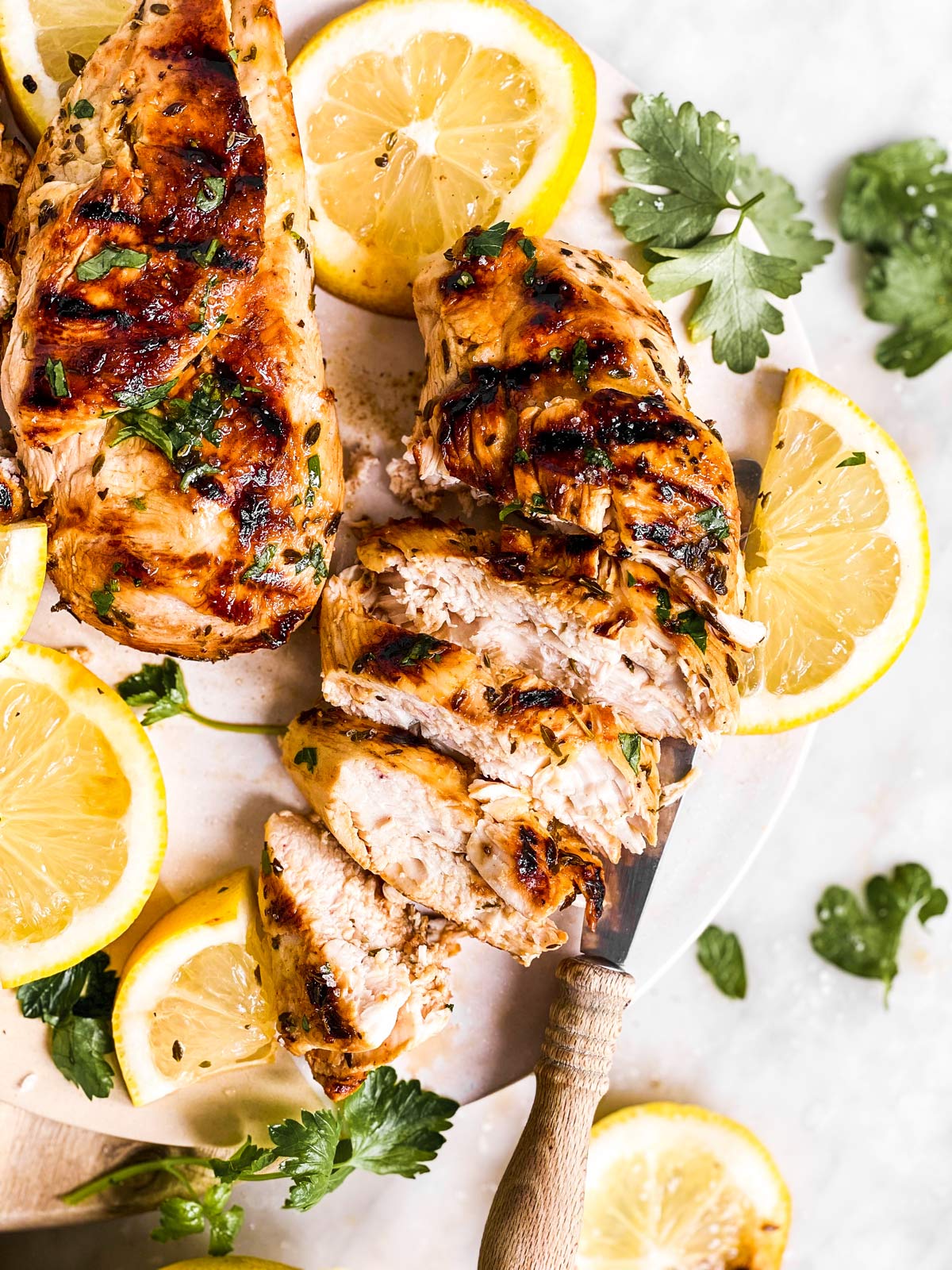 sliced open grilled chicken on platter with fresh parsley and sliced lemons