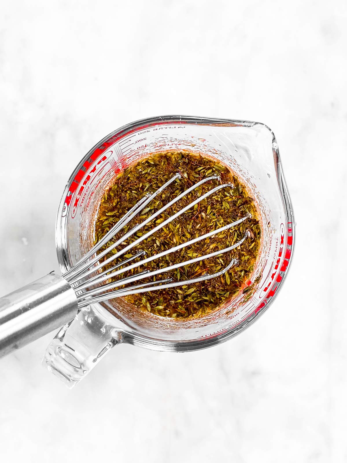 chicken marinade ingredients in glass measuring jug with metal whisk