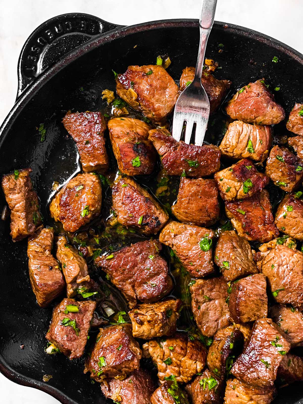 close up photo of steak bites in cast iron skillet, with fork stuck in one piece