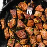 close up photo of steak bites in cast iron skillet, with fork stuck in one piece