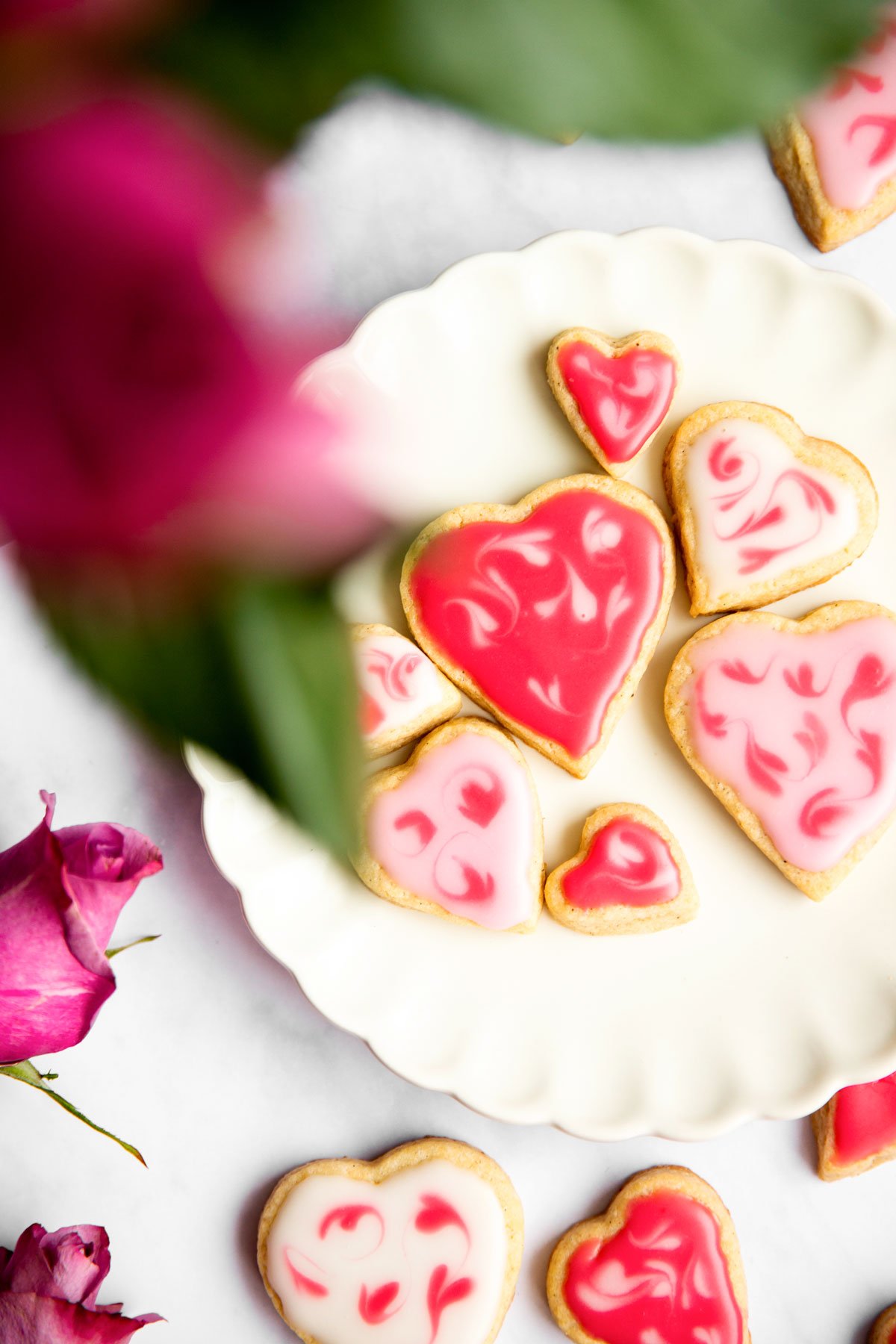 overhead view of white scalloped plate with decorated sugar cookies with pink roses around
