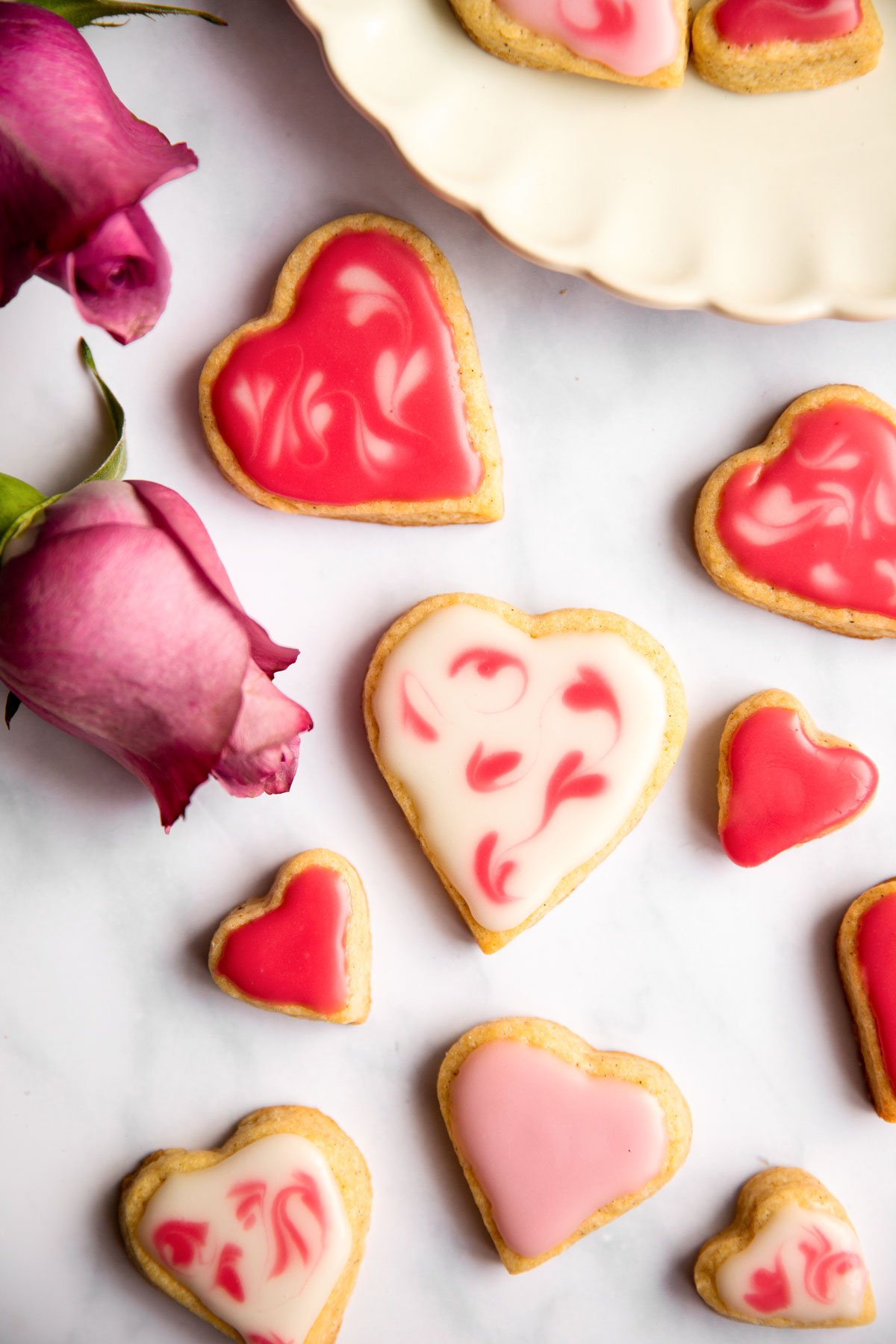 overhead view of valentine's day sugar cookies on marble surface with pink roses