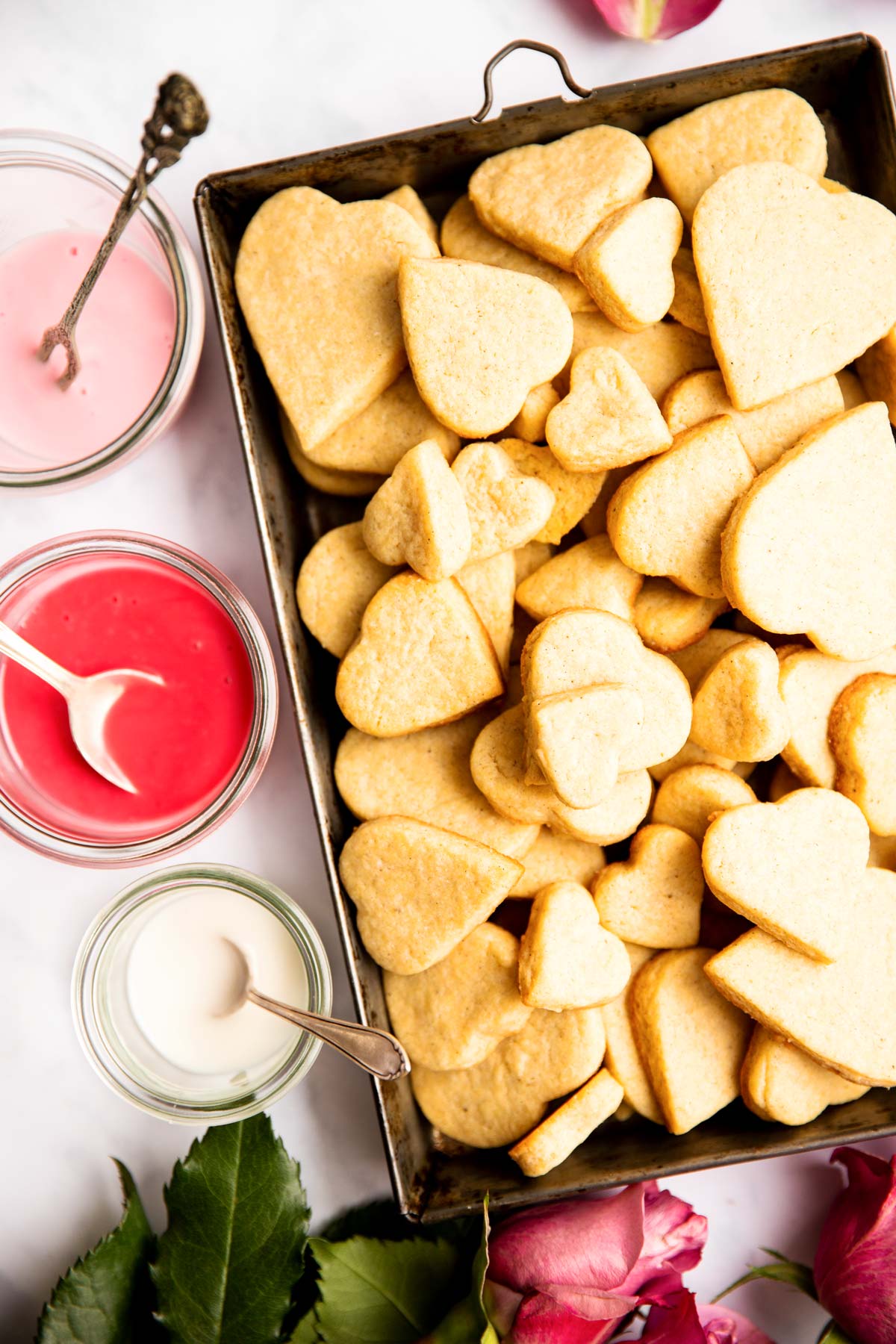 box with heart shaped sugar cookies next to three bowls with colored icing