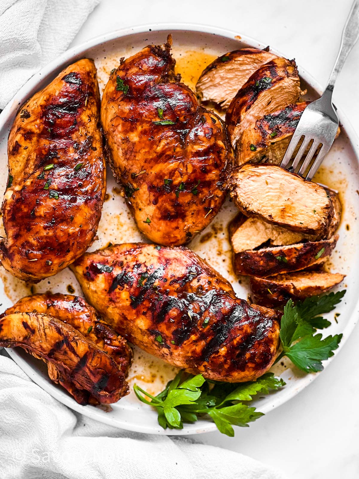 overhead view of four grilled balsamic chicken breasts, one sliced, on white plate