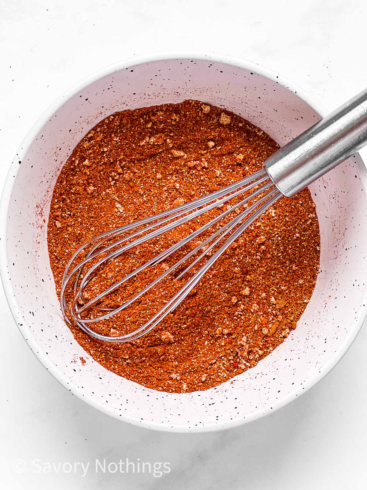 overhead view of BBQ chicken spice rub in small white bowl with metal whisk