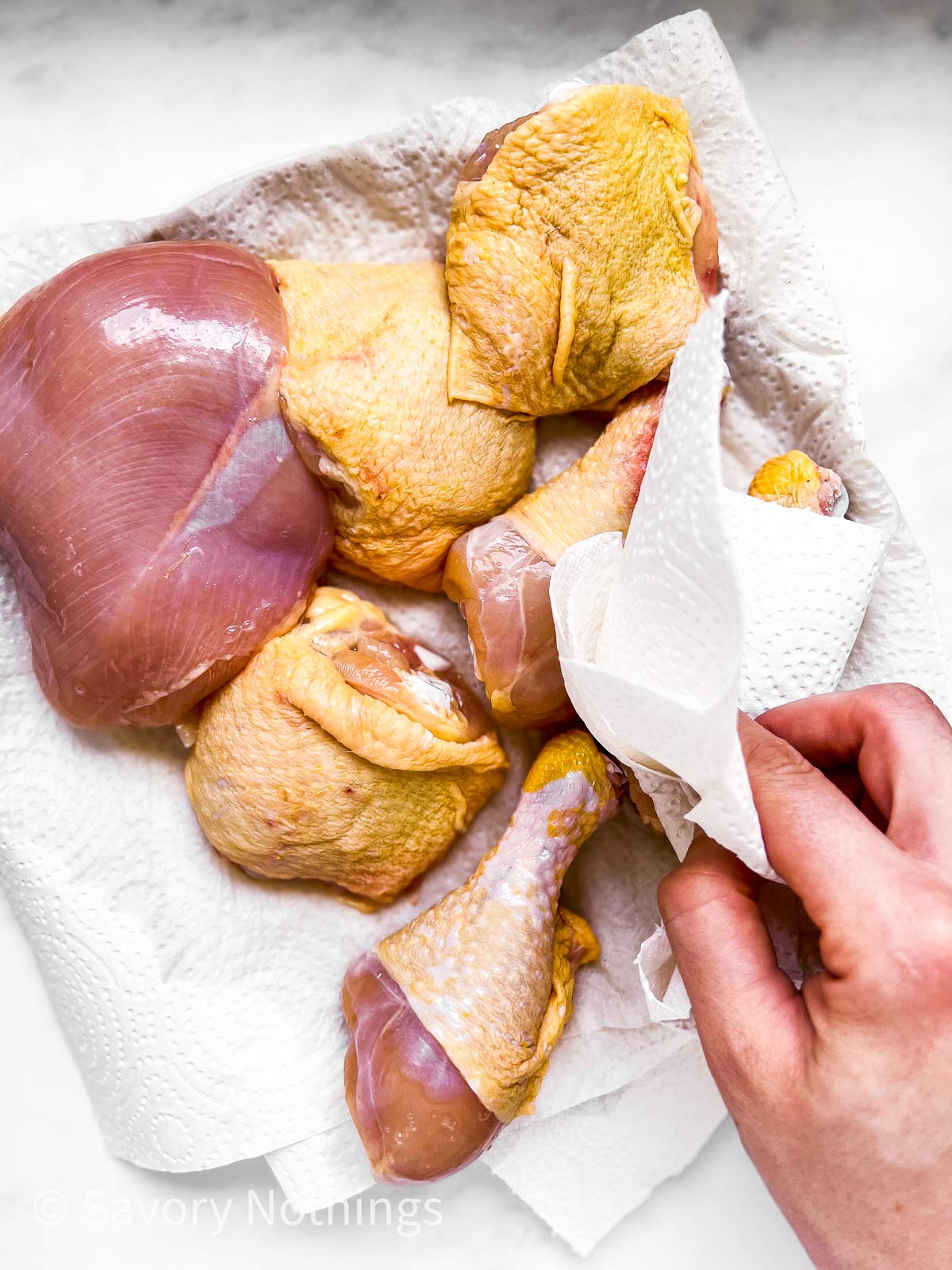 female hand using paper towels to pat dry raw chicken pieces