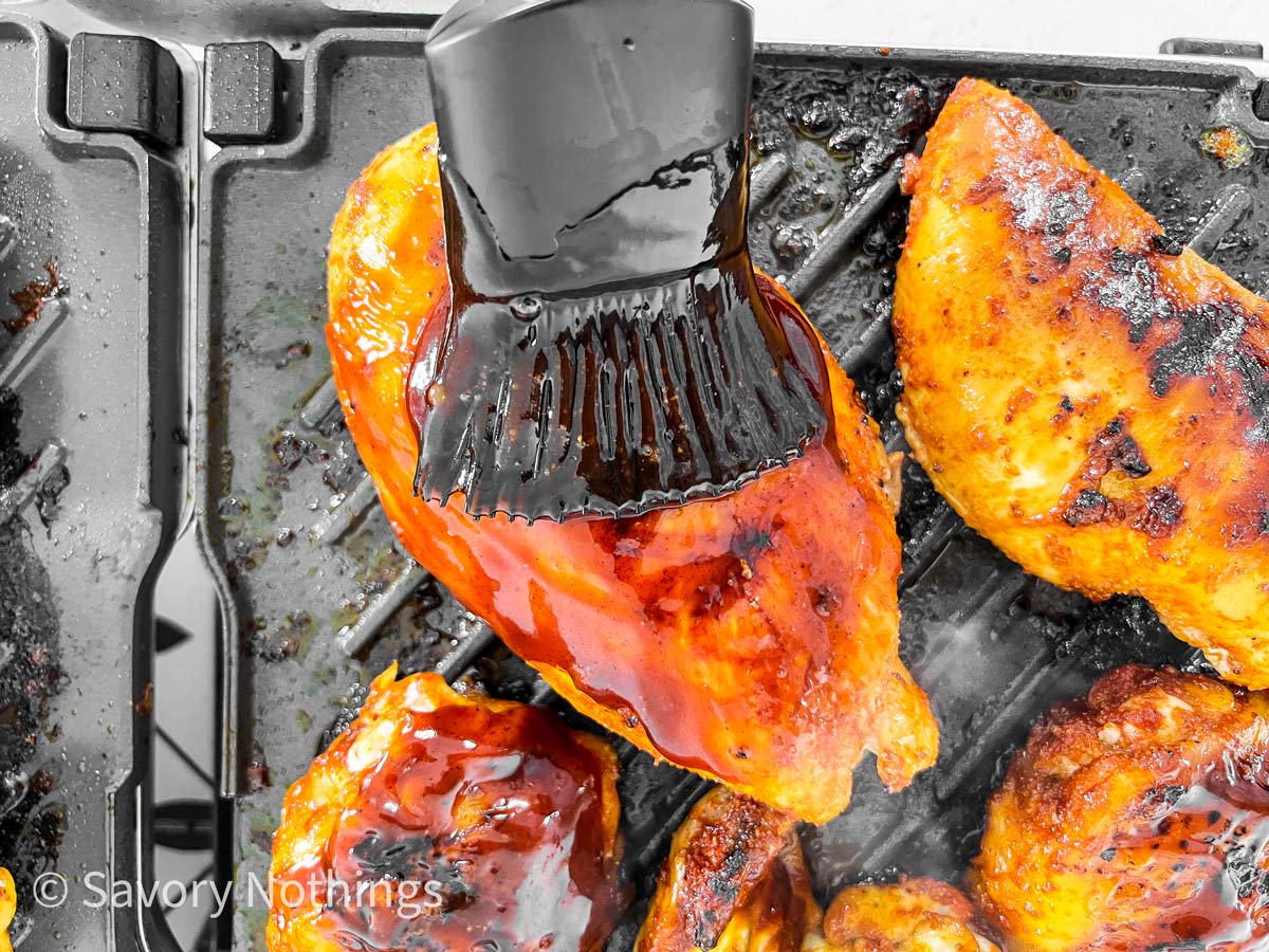 silicone brush brushing BBQ sauce on grilled chicken pieces