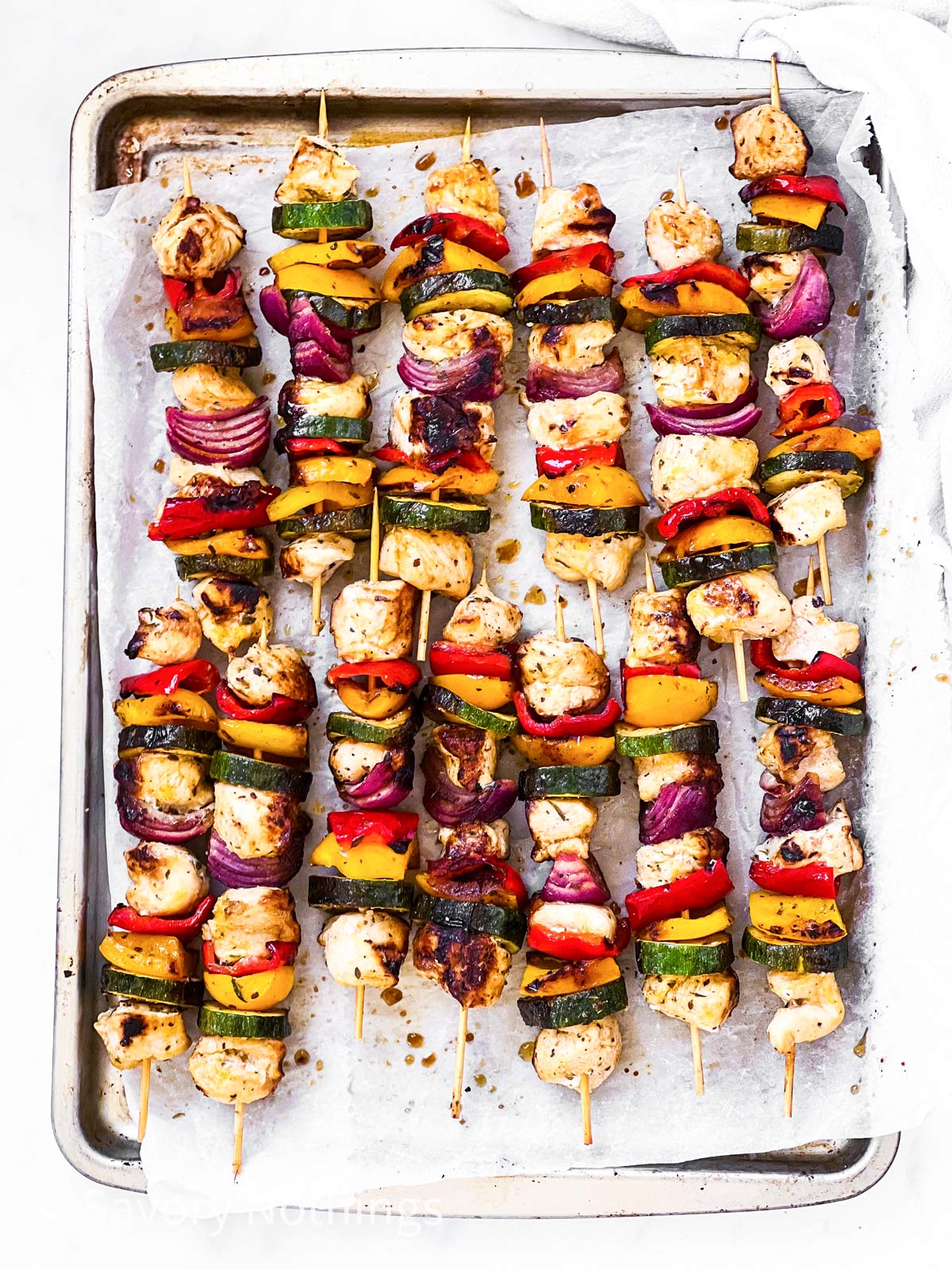 overhead view of grilled chicken skewers on lined baking sheet