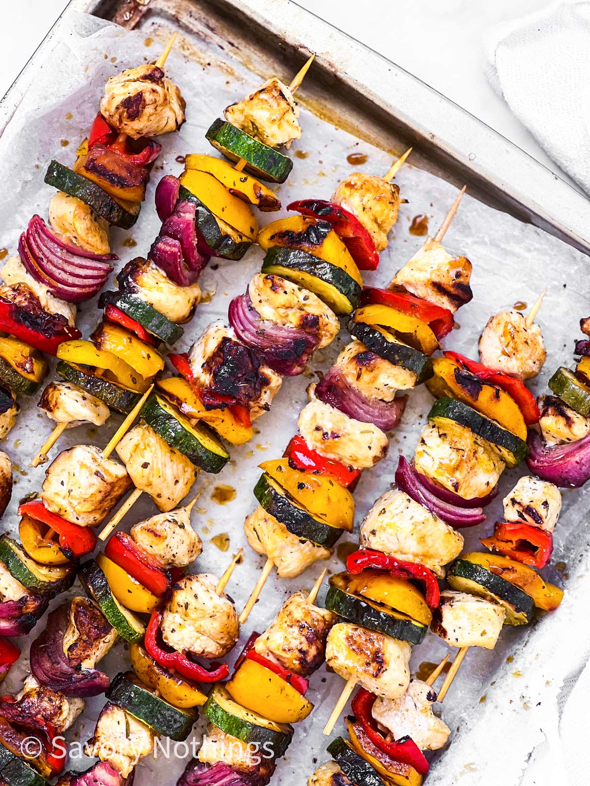 overhead close up view of several Greek chicken kabobs on lined baking tray