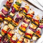 overhead close up view of several Greek chicken kabobs on lined baking tray