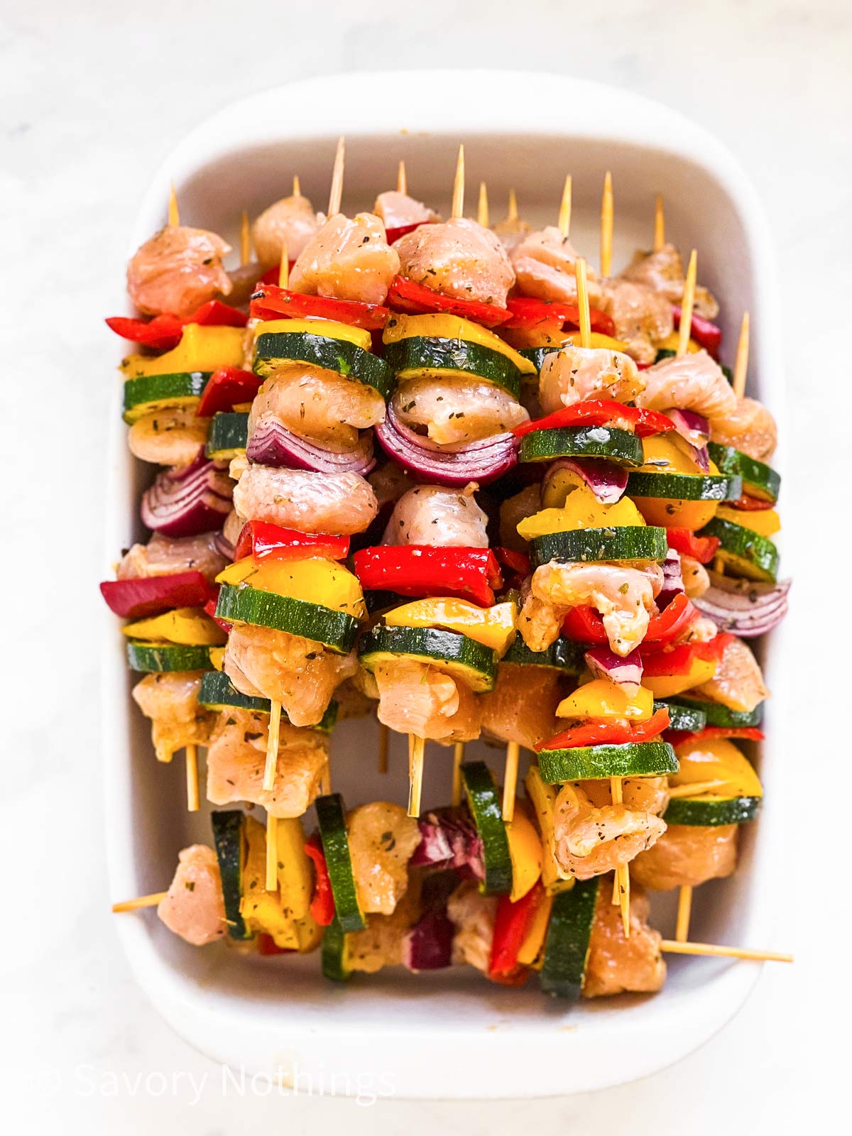 pile of uncooked chicken kabobs in white dish