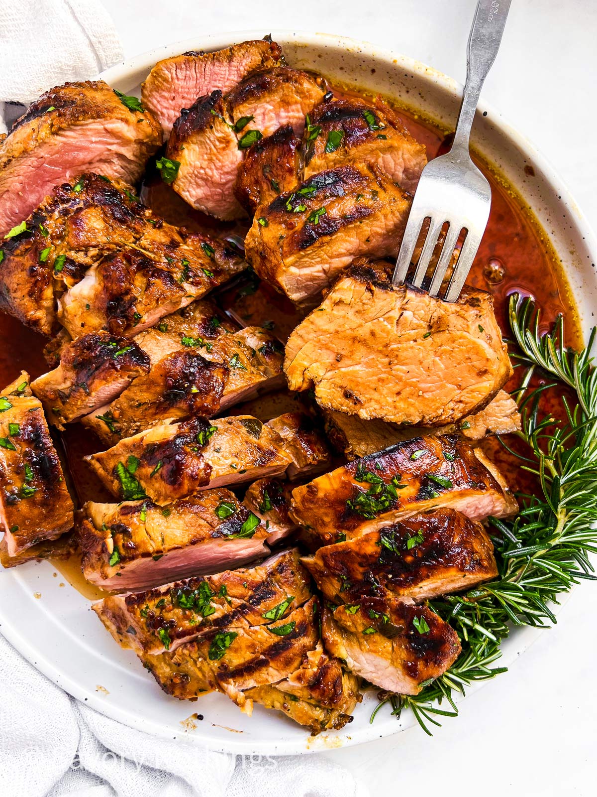 overhead view of marinated, grilled and sliced pork tenderloin on plate with fork