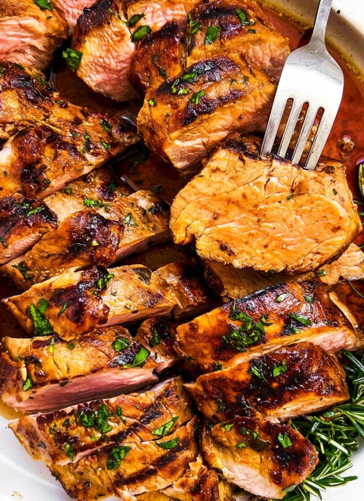 overhead view of marinated, grilled and sliced pork tenderloin on plate with fork
