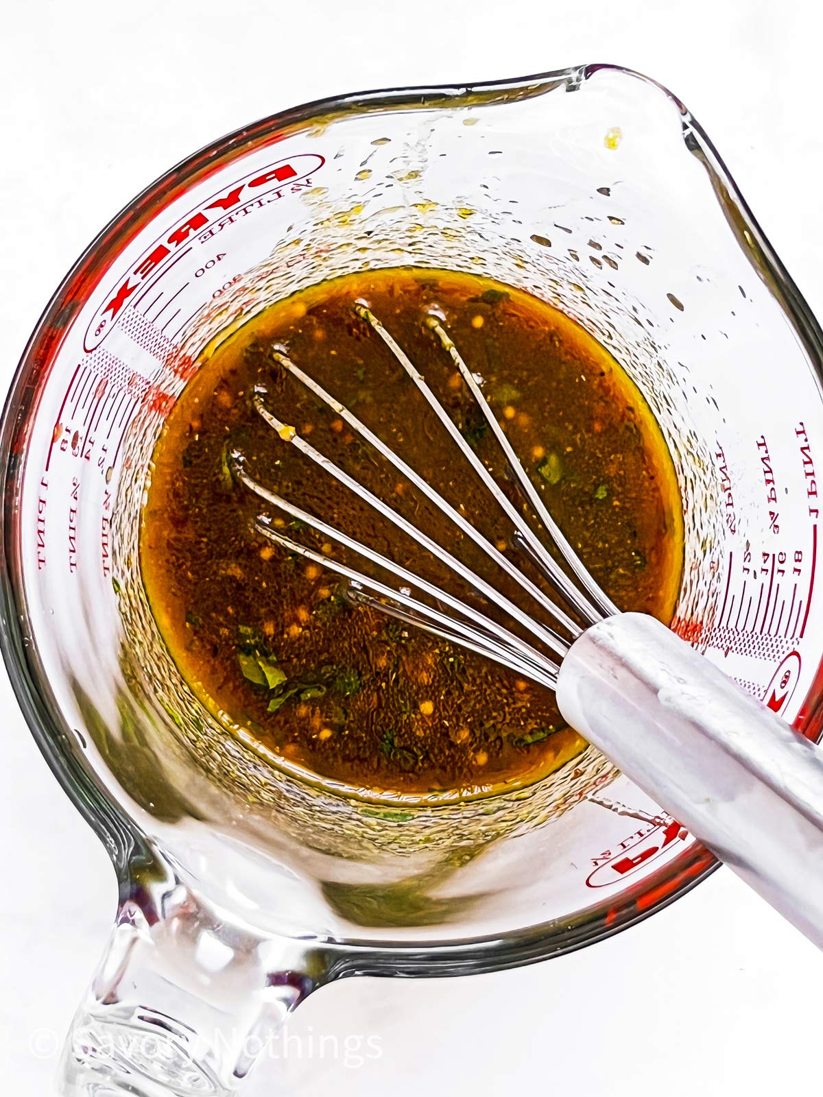 overhead view of pork tenderloin marinade in glass measuring jug with metal whisk