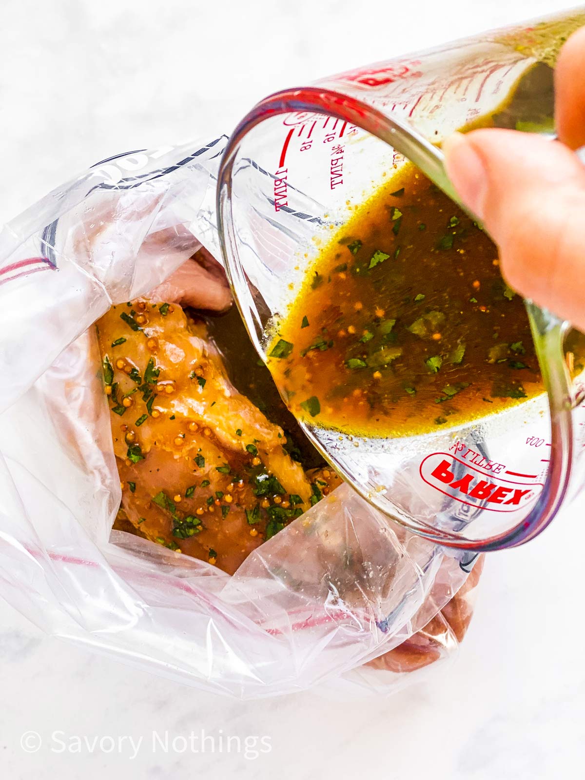 female hand pouring marinade over pork tenderloin in plastic bag