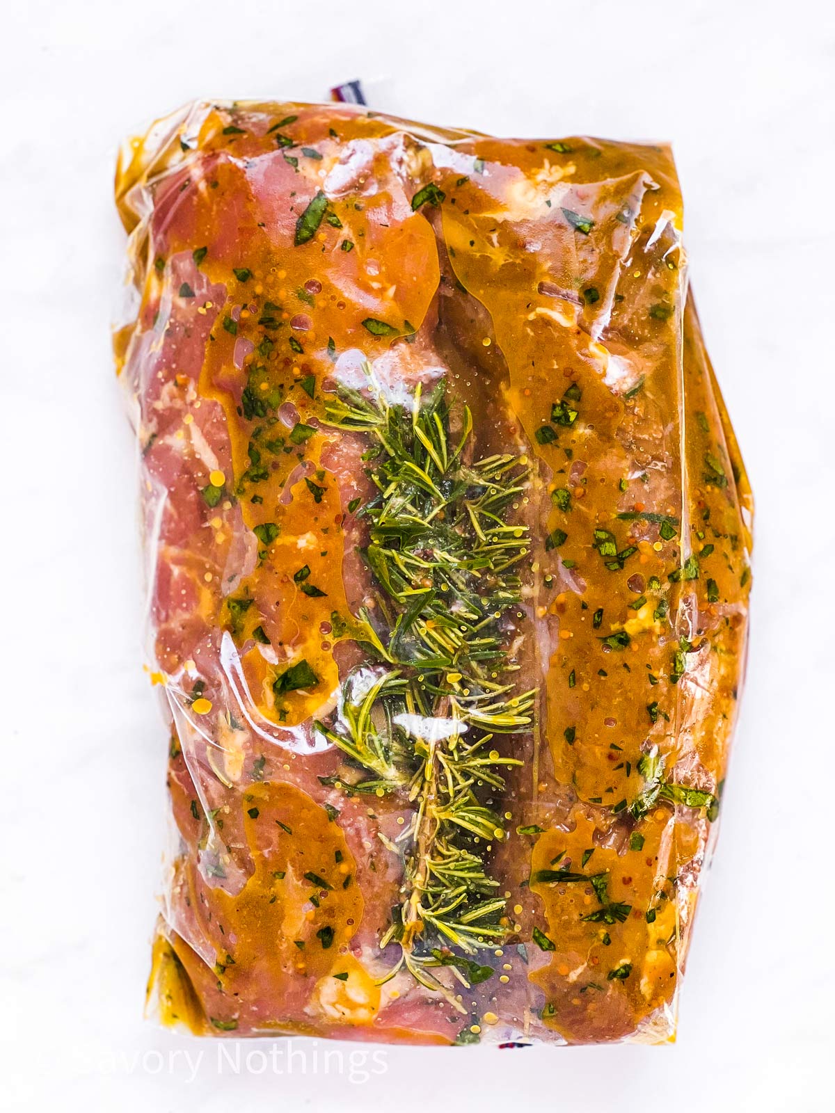 pork tenderloins and rosemary sprig in marinade in zip-top bag