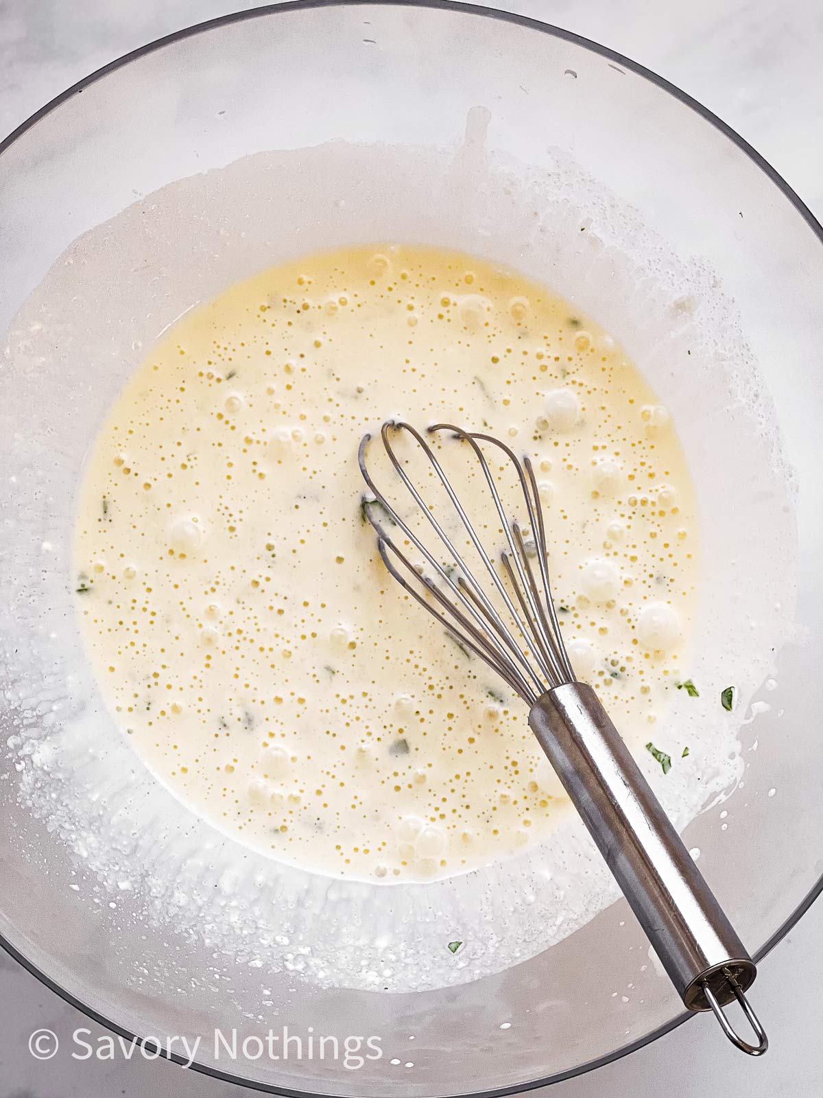 mayonnaise dressing in glass bowl with metal whisk