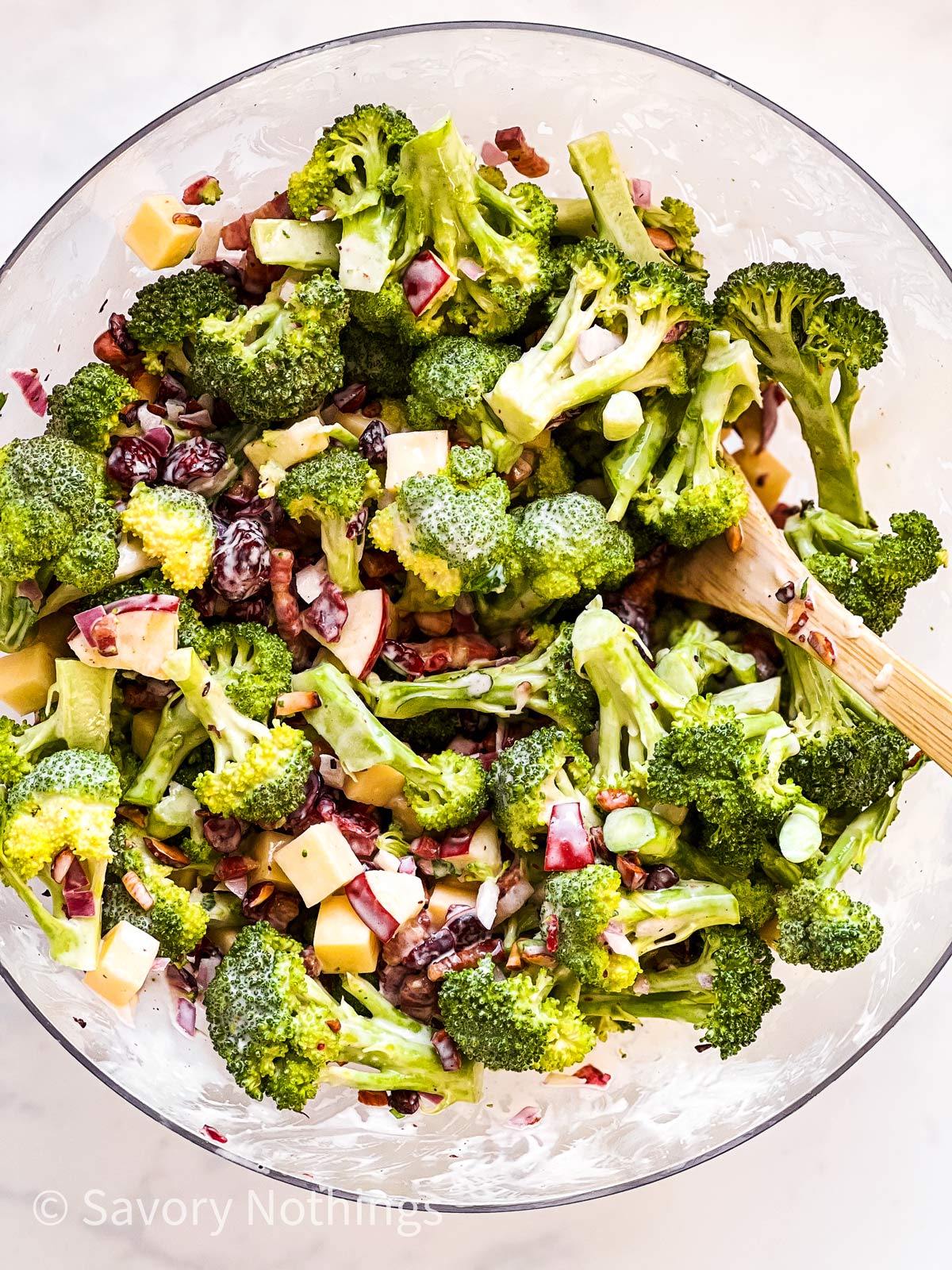 broccoli salad in glass bowl with wooden spoon