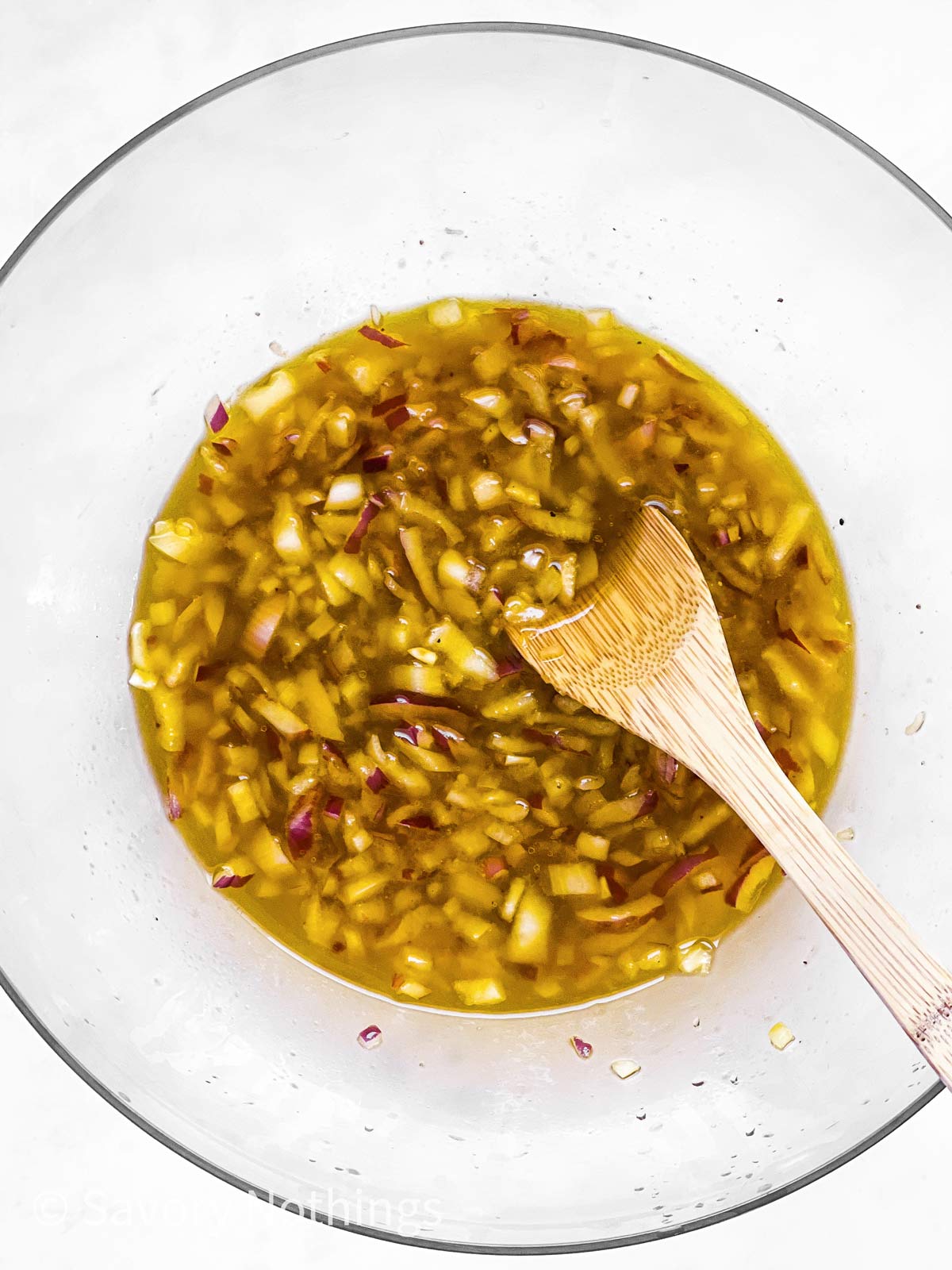 large glass bowl with salad dressing and chopped onion with wooden spoon