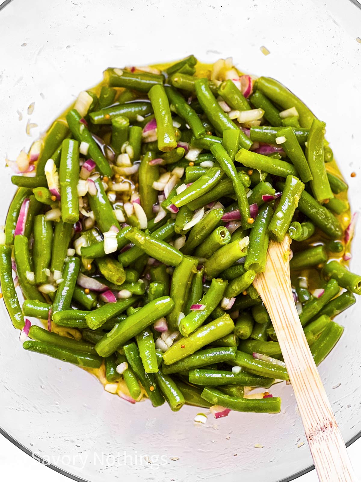green beans and chopped onion in glass bowl, with wooden spoon stuck in