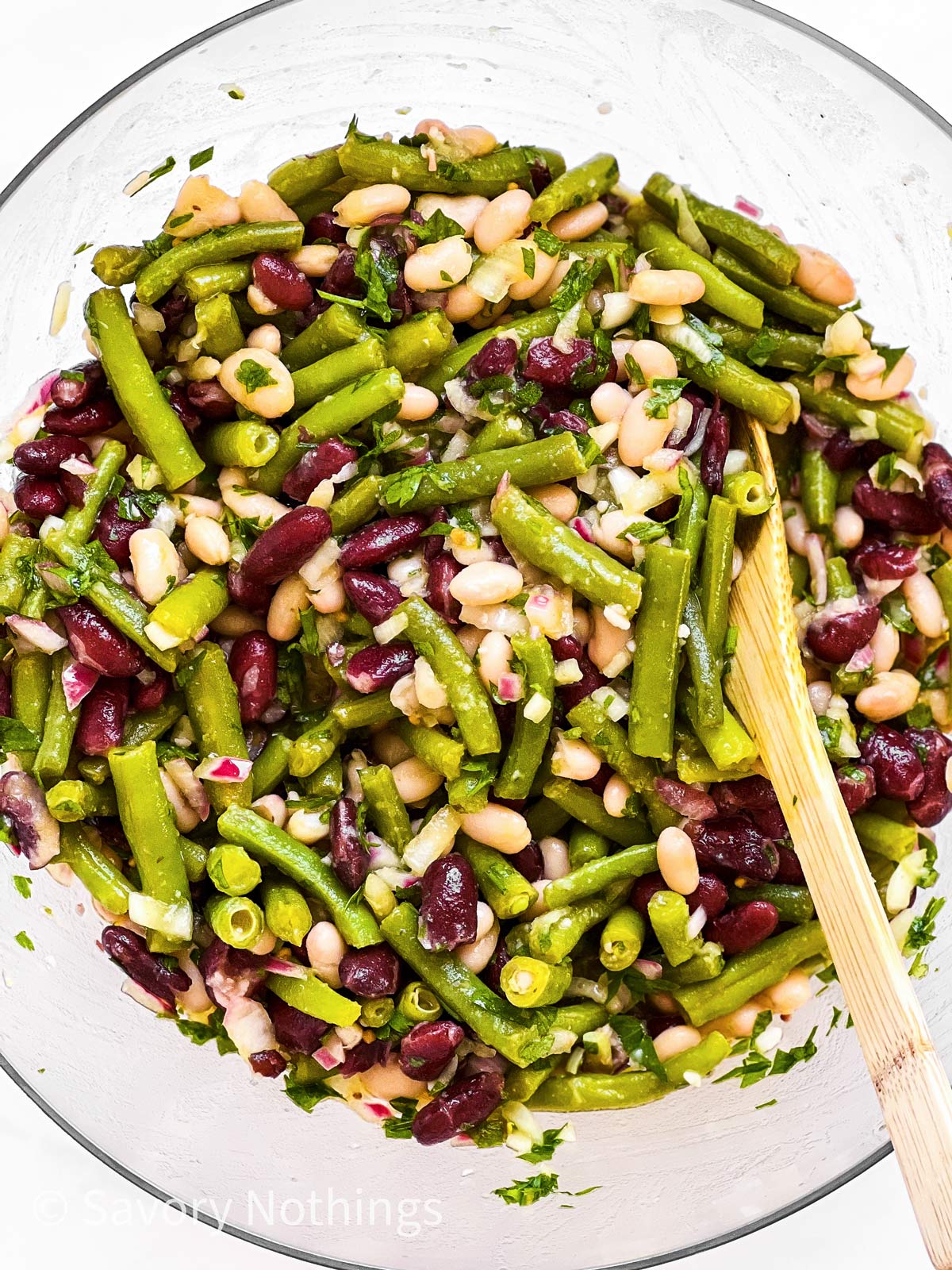 wooden spoon stirring three bean salad in glass bowl