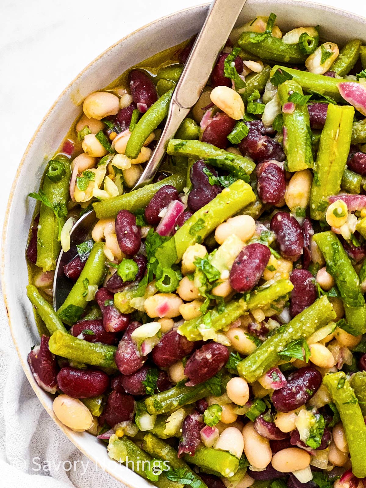 close up photo of three bean salad in white bowl with a spoon